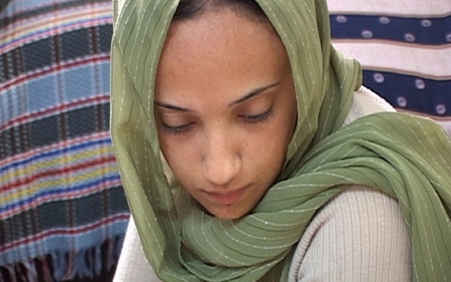 A woman in a green headscarf looks down.