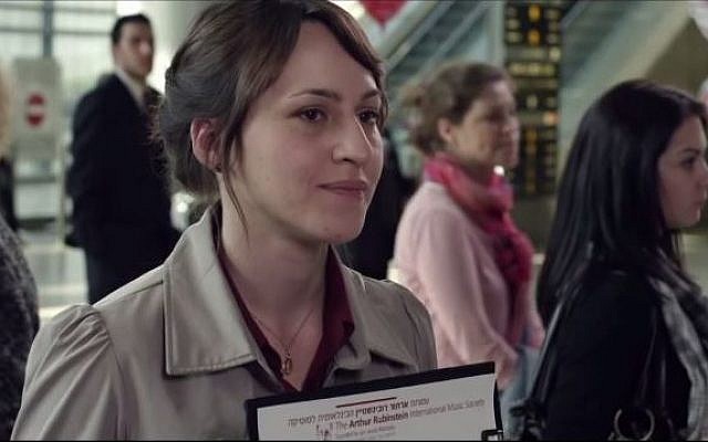 A woman in a brown collared jacket holds up a sign at an airport.